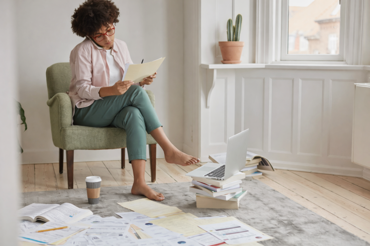Woman sitting in armchair reviewing bills and paperwork scattered on the floor.