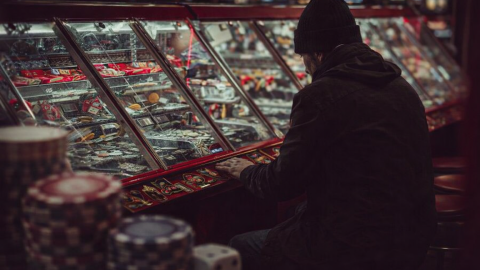 Man sitting alone at a casino machine intensely focused on gambling while surrounded by bright casino lights and gaming machines.