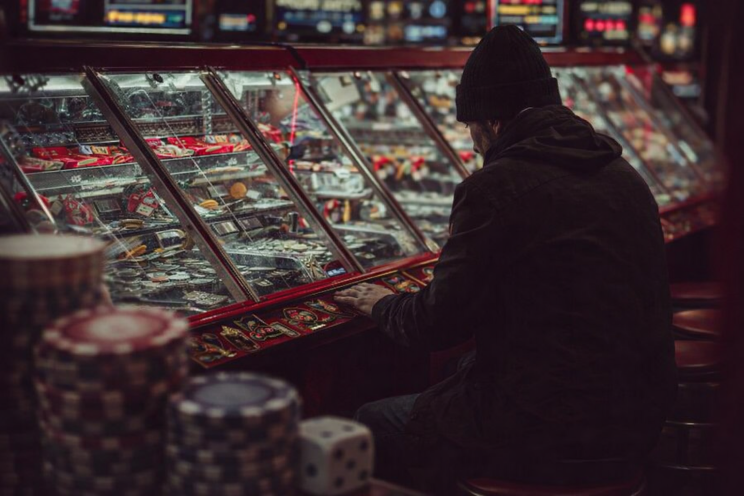 Man sitting alone at a casino machine intensely focused on gambling while surrounded by bright casino lights and gaming machines.