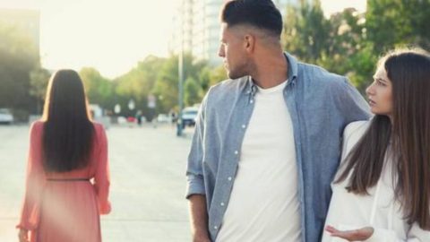 A man in a formal outfit, presumably with his partner, distractedly gazing at a woman passing by.