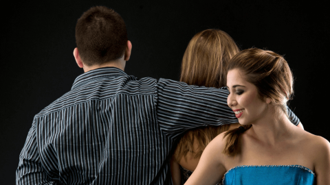 Woman secretly holding hands with another man while standing behind her unsuspecting husband.