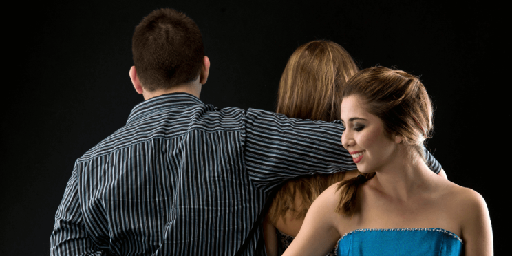 Woman secretly holding hands with another man while standing behind her unsuspecting husband.