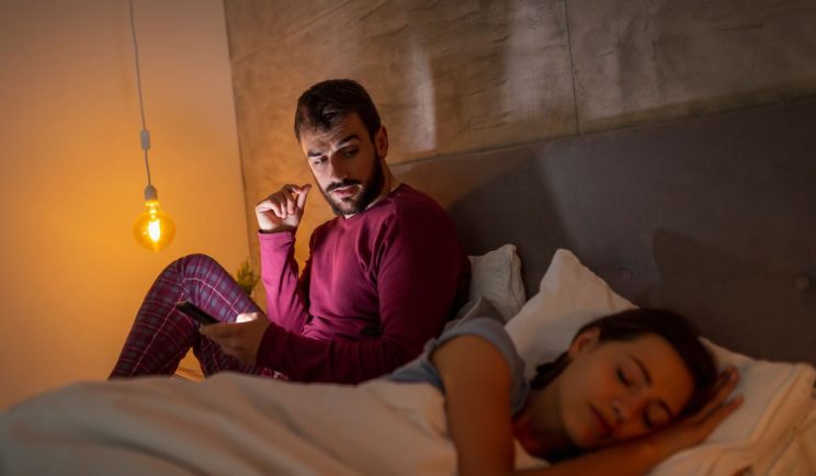 A suspicious partner looking at their spouse’s phone while they’re distracted