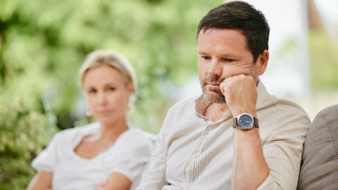 A man deep in thought and emotionally distant sitting beside a woman on a couch