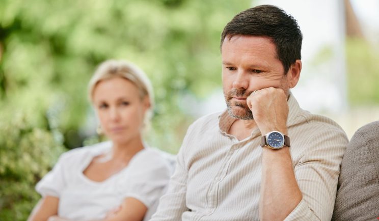 A man deep in thought and emotionally distant sitting beside a woman on a couch