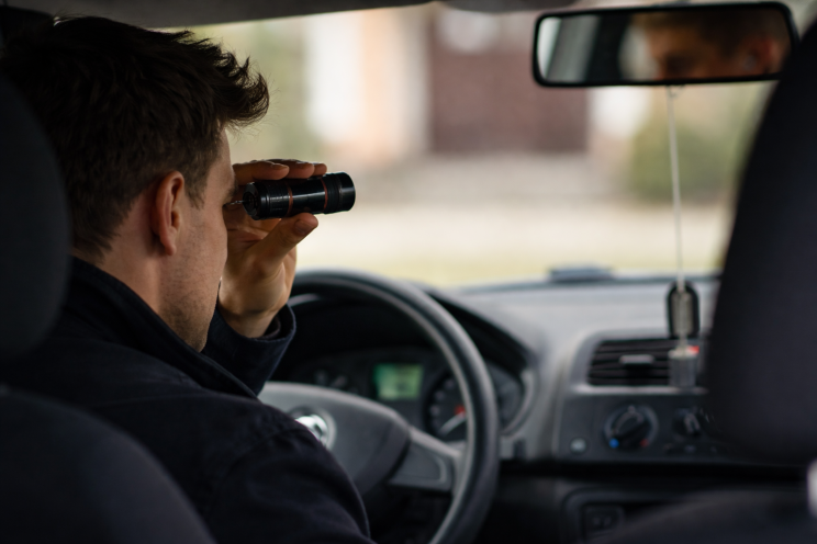Private investigator inside a car observing surroundings discreetly using binoculars in Brisbane Australia